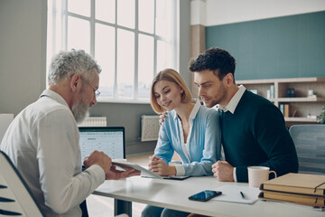 Financial advisor showing digital tablet to his clients while sitting in the office together