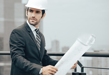 Architect manager holds blueprint standing on rooftop of skyscraper building in the city, portrait. Beard man engineer working at construction site planning building development project. Copy space.