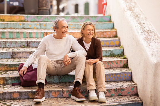 Wall Mural - Happy Senior Tourists Couple Sitting On Colorful Steps Outdoors