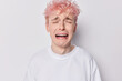 Gloomy upset man with pink hair cries from despair complains about bad life whines desperately feels down depressed wears casual t shirt isolated over white background. Negative human emotions concept
