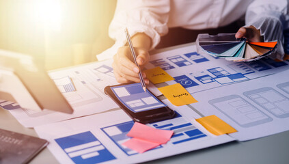 Close up ux developer and ui designer brainstorming about mobile app interface wireframe design on table with customer breif and color code at modern office.Creative digital development agency
