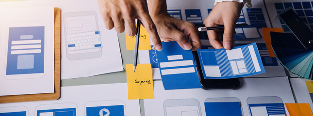 Close up ux developer and ui designer brainstorming about mobile app interface wireframe design on table with customer breif and color code at modern office.Creative digital development agency