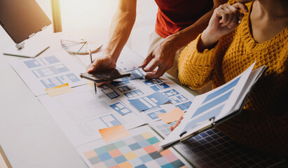 Close up ux developer and ui designer brainstorming about mobile app interface wireframe design on table with customer breif and color code at modern office.Creative digital development agency
