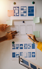 Close up ux developer and ui designer brainstorming about mobile app interface wireframe design on table with customer breif and color code at modern office.Creative digital development agency