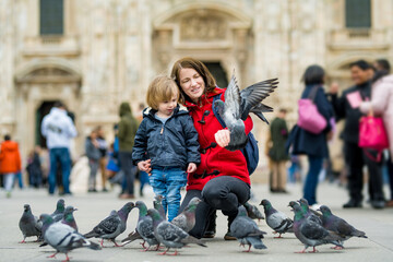 Young mother and her toddler son feeding the pigeons on the Cathedral Square or Piazza del Duomo in the center of Milan, Italy.