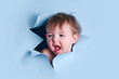 A yawning baby in a hole on a paper blue background. Torn child's head studio background, copy space. Kid aged one year six months