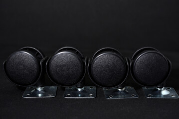 Black plastic furniture rollers on a black background.