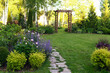summer garden view with stone path, rutic wooden archway, yellow spirea and blooming peonies with catmint
