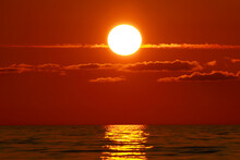 Big Red Sun Setting Over Ocean And Sun Reflection Trail On Water Surface