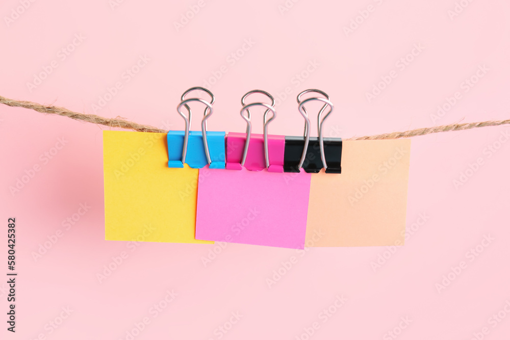 Sticky notes with binder clips hanging on rope against pink background