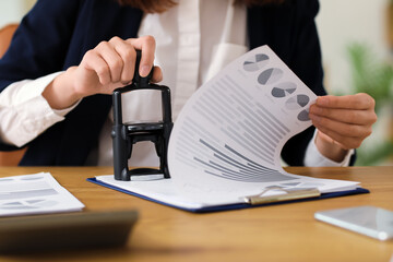 Wall Mural - Female accountant stamping document at table in office, closeup