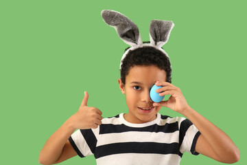 Sticker - African-American little boy in bunny ears with Easter egg showing thumb-up on green background