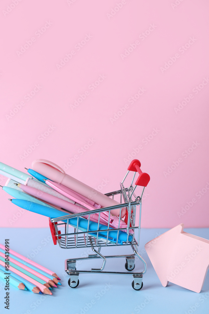 Shopping cart with different pens, pencils and sticky notes on color background