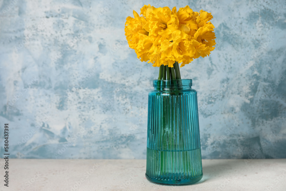 Vase with narcissus flowers on table near grunge wall