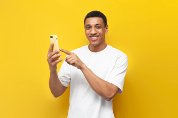 young african american man in white t-shirt uses smartphone and presses his finger on the screen on yellow background