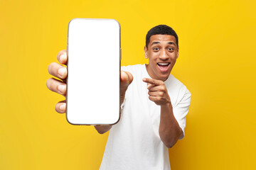 Wall Mural - young african american guy in white t-shirt shows blank screen of smartphone on yellow isolated background