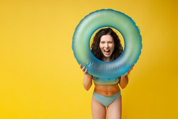 Wall Mural - young shocked brunette girl in summer in a blue swimsuit holds an inflatable swimming ring and screams