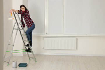 Poster - Young beautiful woman with roller on metal stepladder indoors. Room renovation