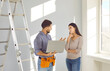 © Studio Romantic - Repairman with modern laptop talking to young homeowner girl. Male worker with tool belt standing by step ladder, holding notebook computer and explaining to woman what he has to repair in the house