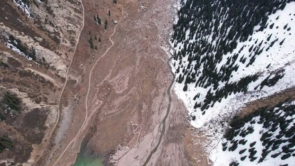 Wall Mural - A lake in the mountains with turquoise blue water. Drone view of clear water, coniferous trees and snowy mountains. People walk along the shore, low bushes grow. Big Almaty lake. Kazakhstan