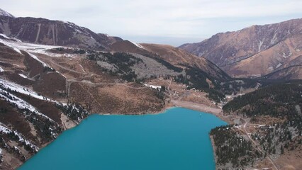 Wall Mural - A lake in the mountains with turquoise blue water. Drone view of clear water, coniferous trees and snowy mountains. People walk along the shore, low bushes grow. Big Almaty lake. Kazakhstan