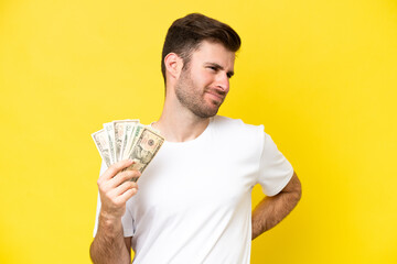 Wall Mural - Young caucasian man taking a lot of money isolated on yellow background suffering from backache for having made an effort