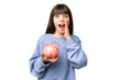© luismolinero - Little girl holding a piggybank over isolated chroma key background shouting with mouth wide open