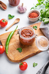 Wall Mural - Homemade tomato sauce for pizza or pasta in a jar on a wooden board on a light background with fresh vegetables and herbs.