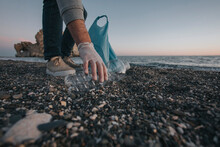 Hand of man picking up plastic bottle on beach
