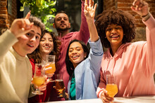 Happy Multiracial Friends With Hands Raised Enjoying At Restaurant