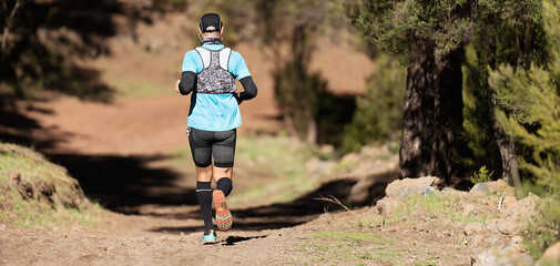 Wall Mural - Athlete man running mountain marathon along a forest trail with a backpack