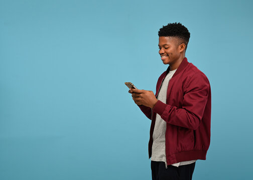 portrait of happy handsome black man using smartphone in cozy studio at home standing on blue backdr