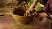 An Asian Woman Puts The Final Touch On A New Clay Bowl, Turning It On A Foot-powered Wheel, Showcasing The Traditional Art Of Pottery-making.