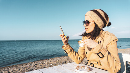 Young woman surfing on the internet and drinking coffee at beach. Empty blank copy space on turquoise sky.