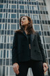 © dsheremeta - Fashion street style portrait of a beautiful girl in a black suit. A beautiful brunette poses against the background of high-rise buildings in the city.