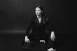 © dsheremeta - Portrait of a modern stylish woman. A brunette in a suit and hat poses barefoot on a black background. BW photo.
