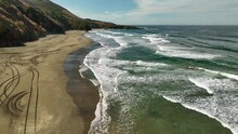 Aerial View Of California's Sandy Coastline With White Crested Waves Rolling Into The Shore.