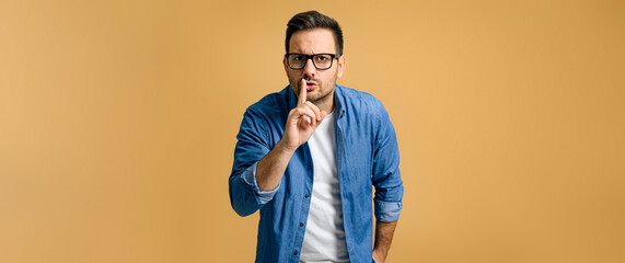 serious mid adult man dressed in blue denim shirt with finger on lips showing silence gesture while 