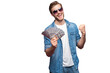 © opolja - Portrait of joyful man in jeans shirt holding bunch of money banknotes while standing and celebrating isolated over transparent background