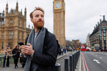 Portrait Of A Stylish Bearded Man With A Smartphone In His Hands Looking To The Side Against The Backdrop Of Big Ben Tower