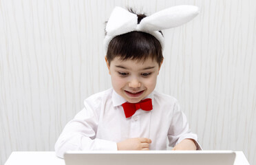 pre schooler boy with bunny rabbit ears headband and red bow at neck isolated pointing with finger up wow amazed shocked expression.child kid in baby crib or at table desk using laptop smiling easter