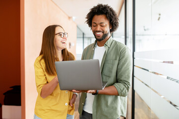 Office employees is meeting together, looking at each other in front of the laptop and discussing. Two colleagues discussing during coffee break, coworkers have friendly conversation. Teamwork concept