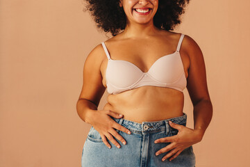 Wall Mural - Happy young woman wearing a bra and jeans in a studio