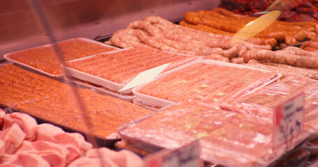 Wall Mural - Minced meat in plastic containers in a window shop. Many packs of raw sausages from diverse animal meat for sale.