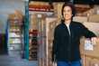 © Jacob Lund - Cheerful warehouse manager standing next to a stack of cardboard boxes