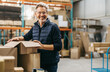 © Jacob Lund - Mature man smiling at the camera while packing cardboard boxes in a warehouse
