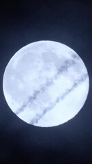 Wall Mural - Airplane crossing the moon at night with trail. Telephoto view of a passenger jet flying against the bright full moon on the mysterious cloudy sky. Plane silhouette, black background and copy space.