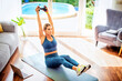 © gzorgz - Sporty woman using dumbbells and laptop while exercising at home