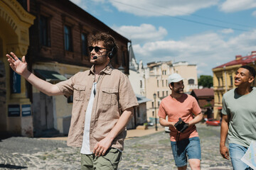 Wall Mural - young guide in headset and sunglasses pointing with hand during excursion with interracial men on po