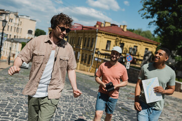 Wall Mural - young tour guide in sunglasses and headset walking with cheerful multicultural tourists on andrews d